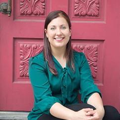 Professor Rachel Uppgaard-Penaz sits on a step in front of an ornate maroon door